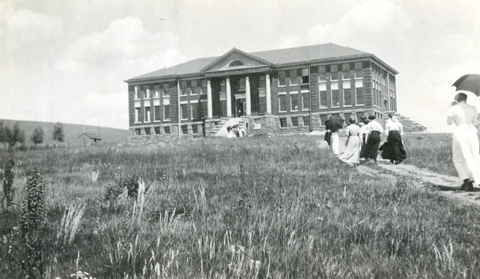 Members of the 1911 student body march up a dirt path through the weeds to Taylor Hall.