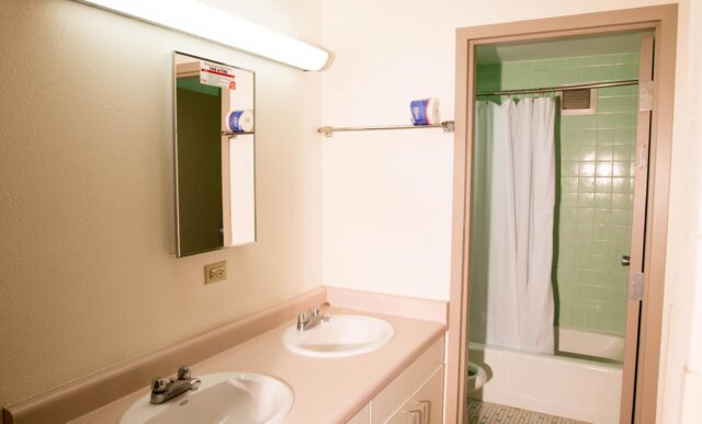 The interior of the Mears Complex shared bathrooms with two sinks in the foreground and a shower in the back.