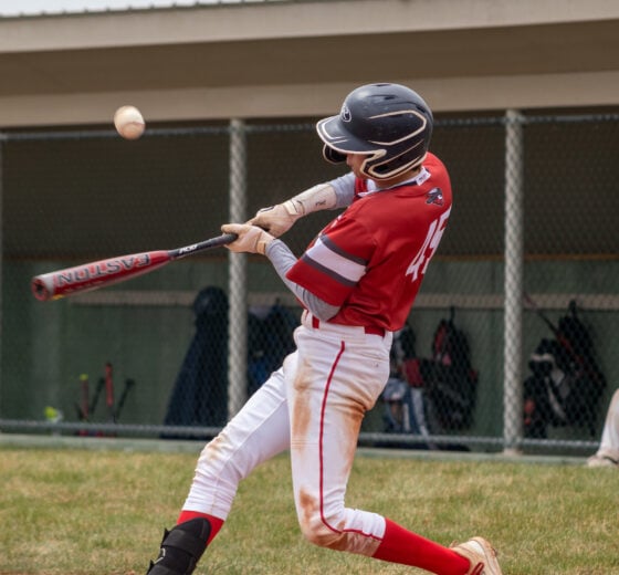 An athlete wearing a baseball uniform and helmet swings at a ball.
