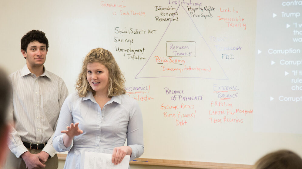 A student delivers a presentation to professor and classmates.