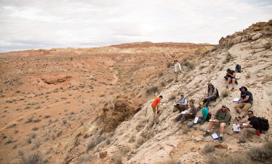 Geology students work on the hillside of a desert landscape.
