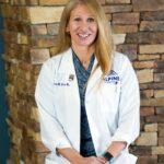 Dr. Gloria Beim smiles at the camera in front of a stone wall. 