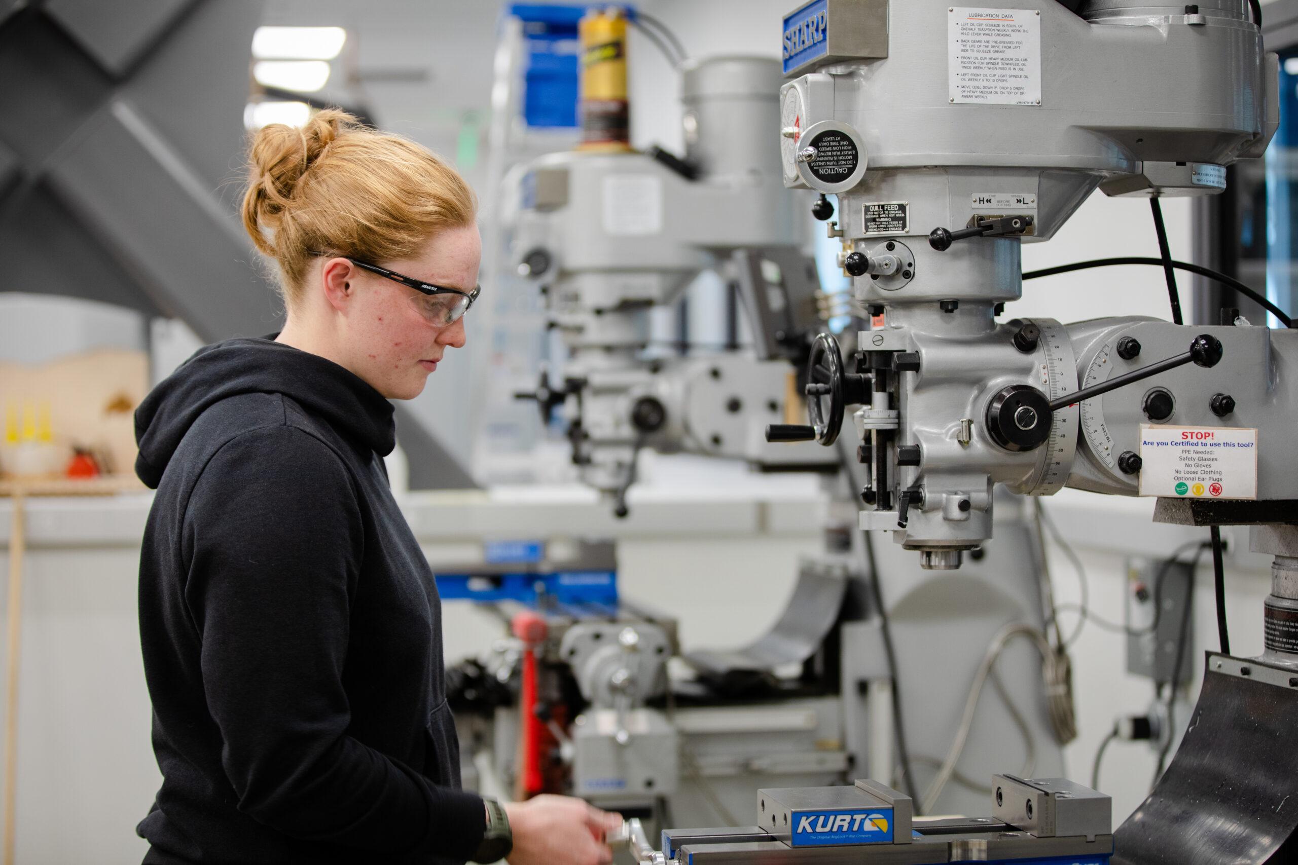 Engineering student, Carolyn Goodwin, wears safety glasses and uses a machine in one of the shops in the Rady Building.