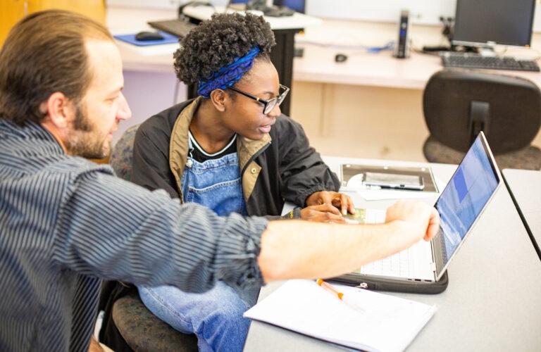 A student gets feedback from a professor during a computer science course.