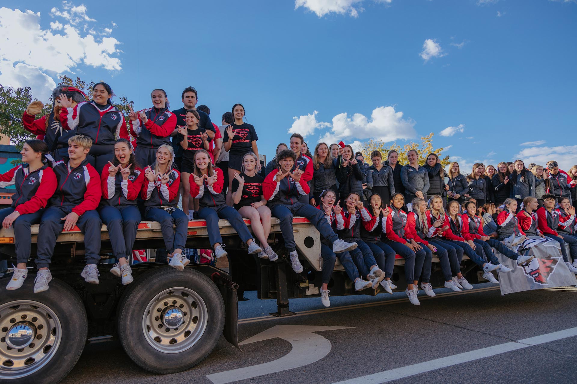 NCAA athletes are lined up on a semi truck bed during the Homecoming Parade.