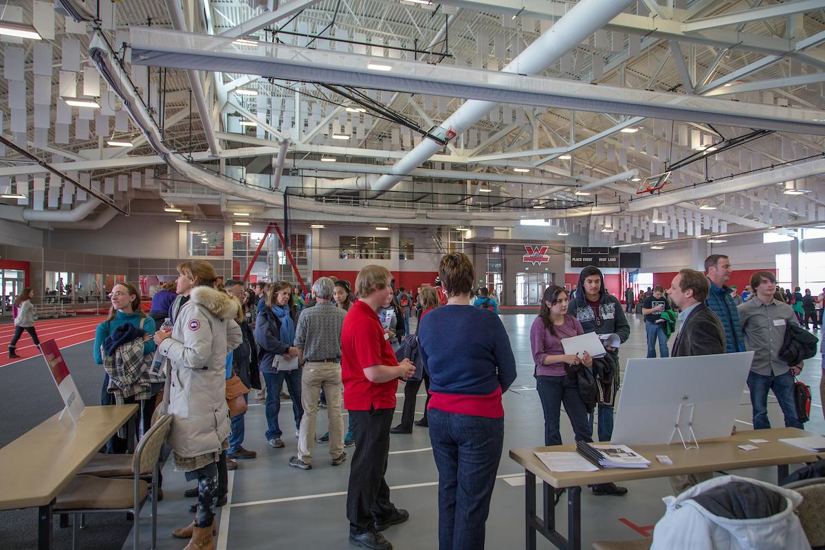 Open house for college: students gather in gym to browse information tables for Preview Day