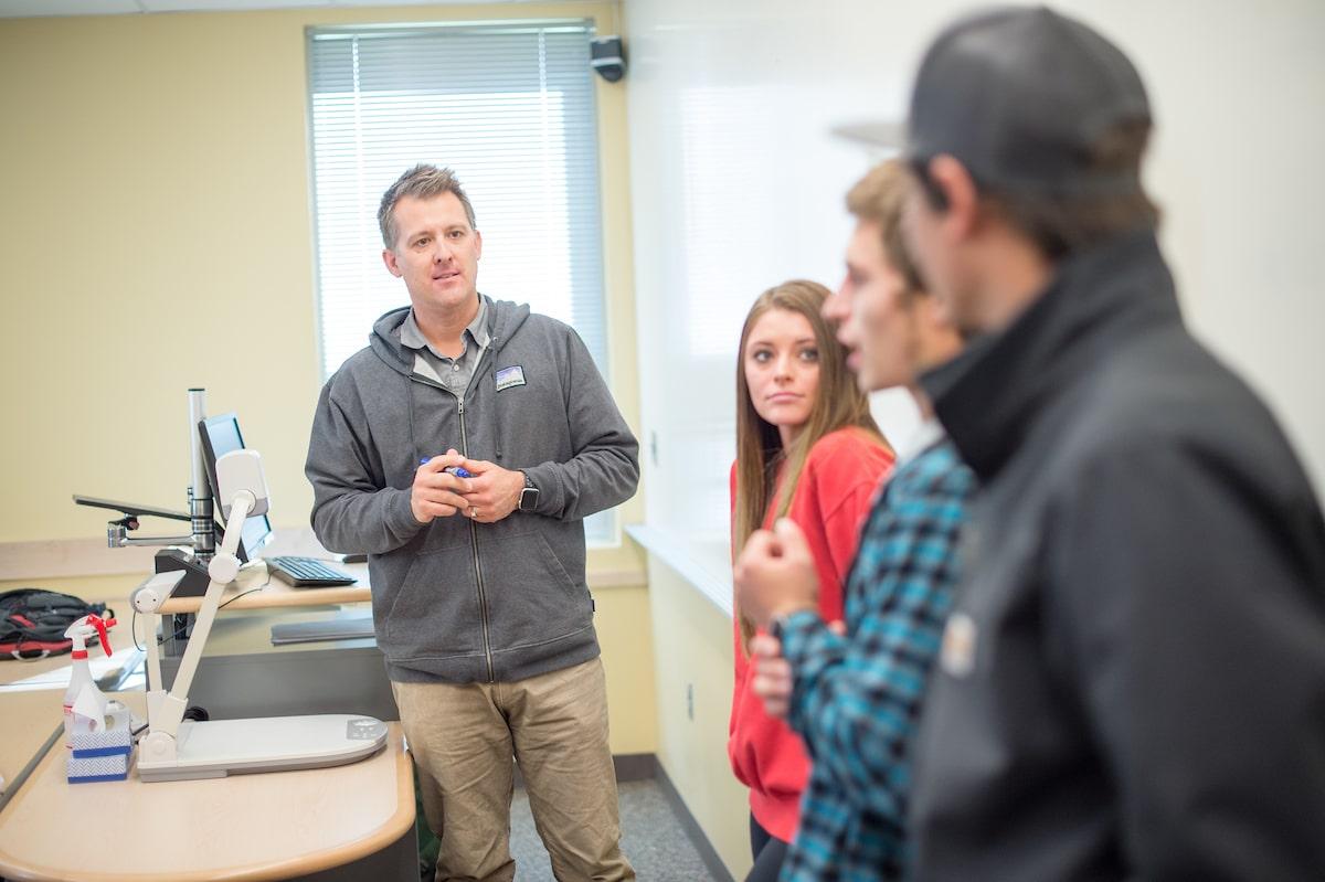 Small class sizes: professor speaking with three students in front of classroom