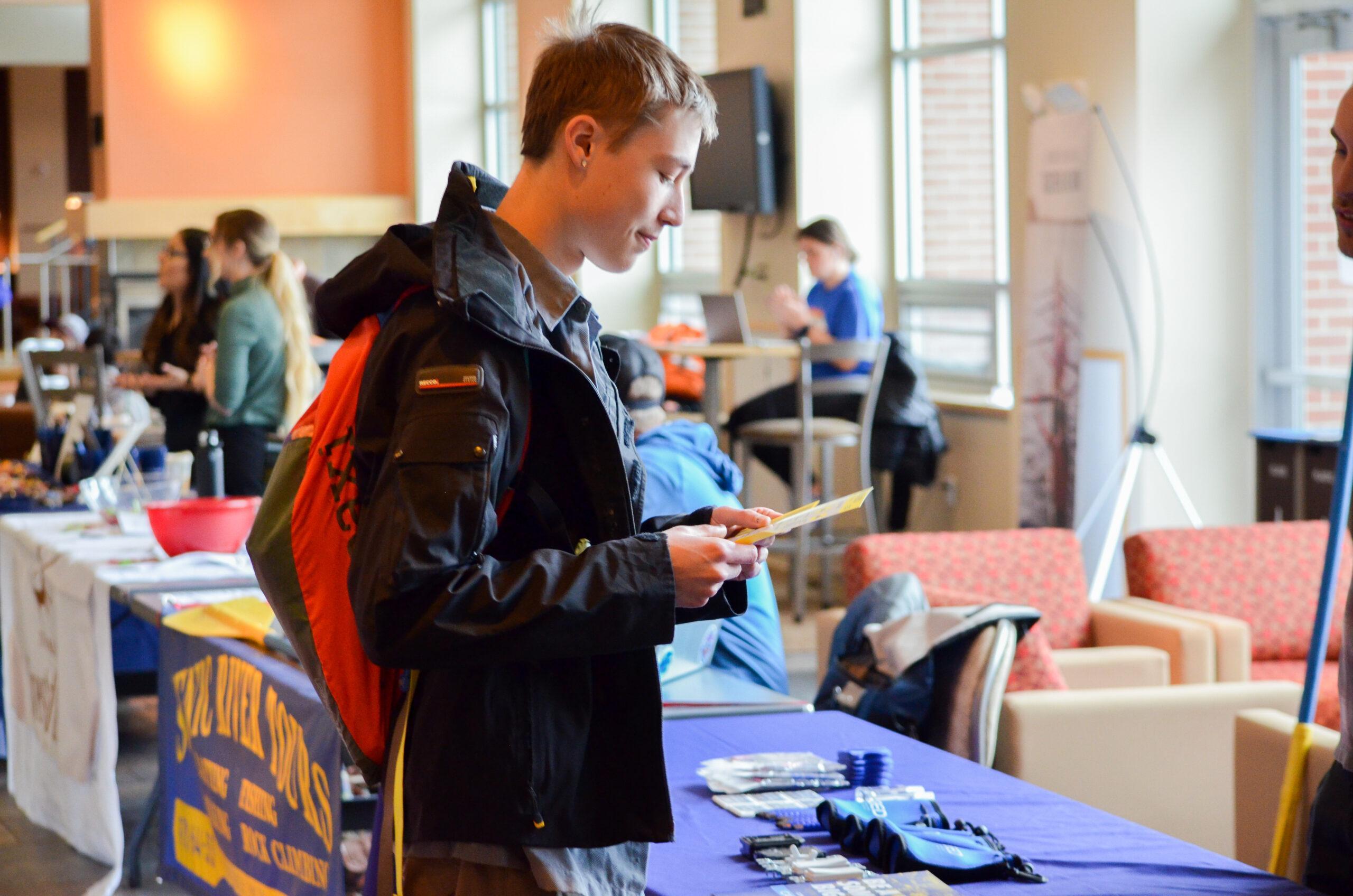 A student holds a pamphlet while talking with an employer at a career fair.