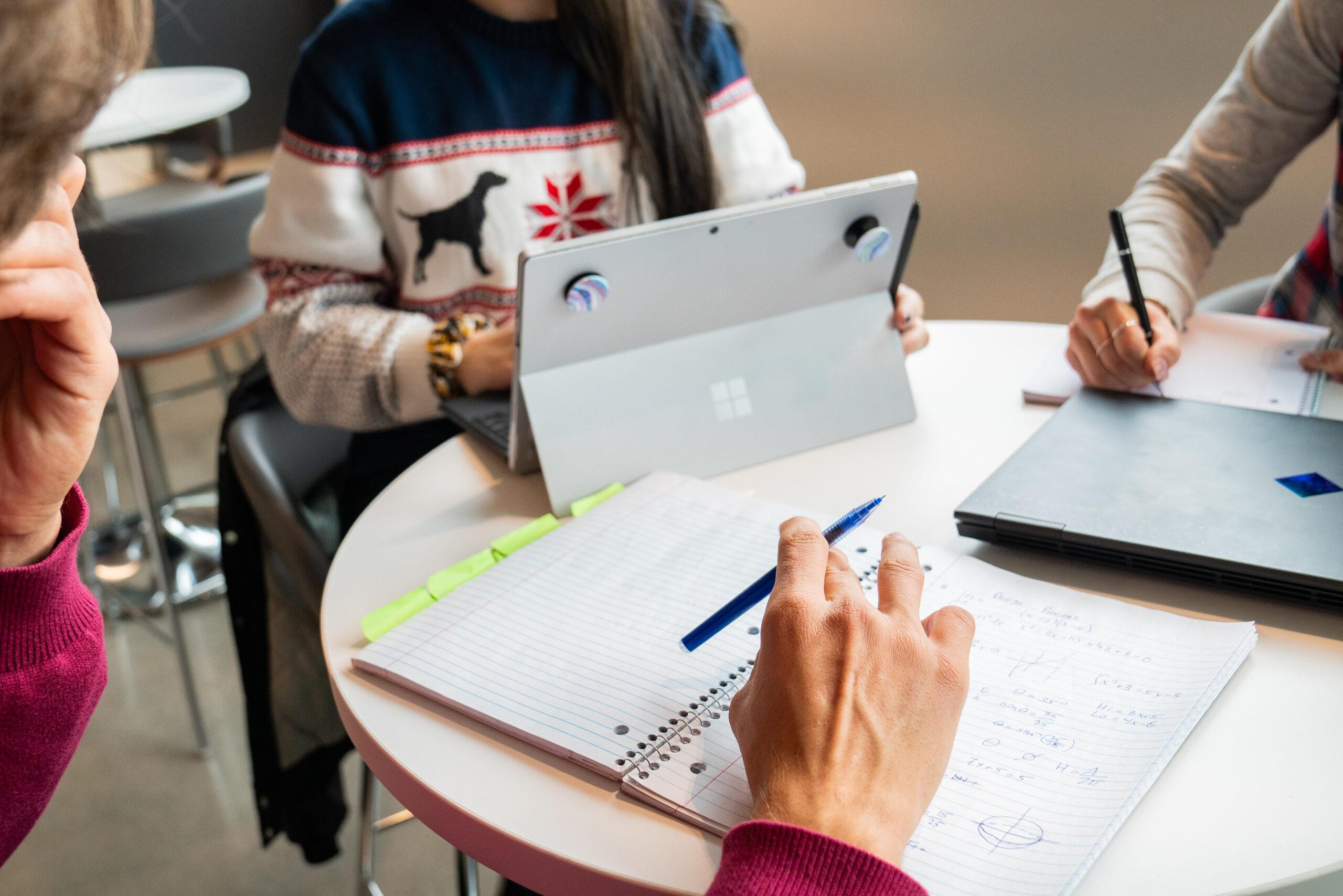 Closeup photo of several students working on homework assignments at a table