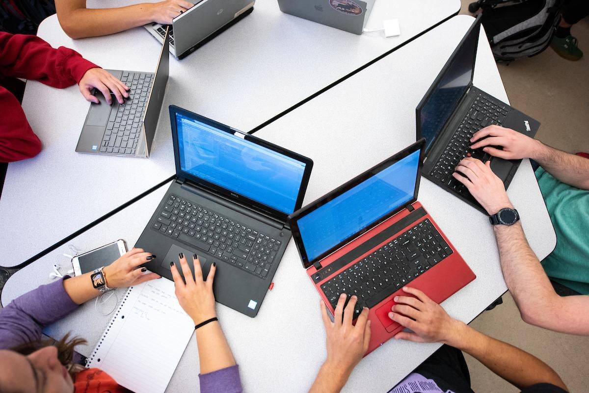 Several students type on laptops in a computer science course.