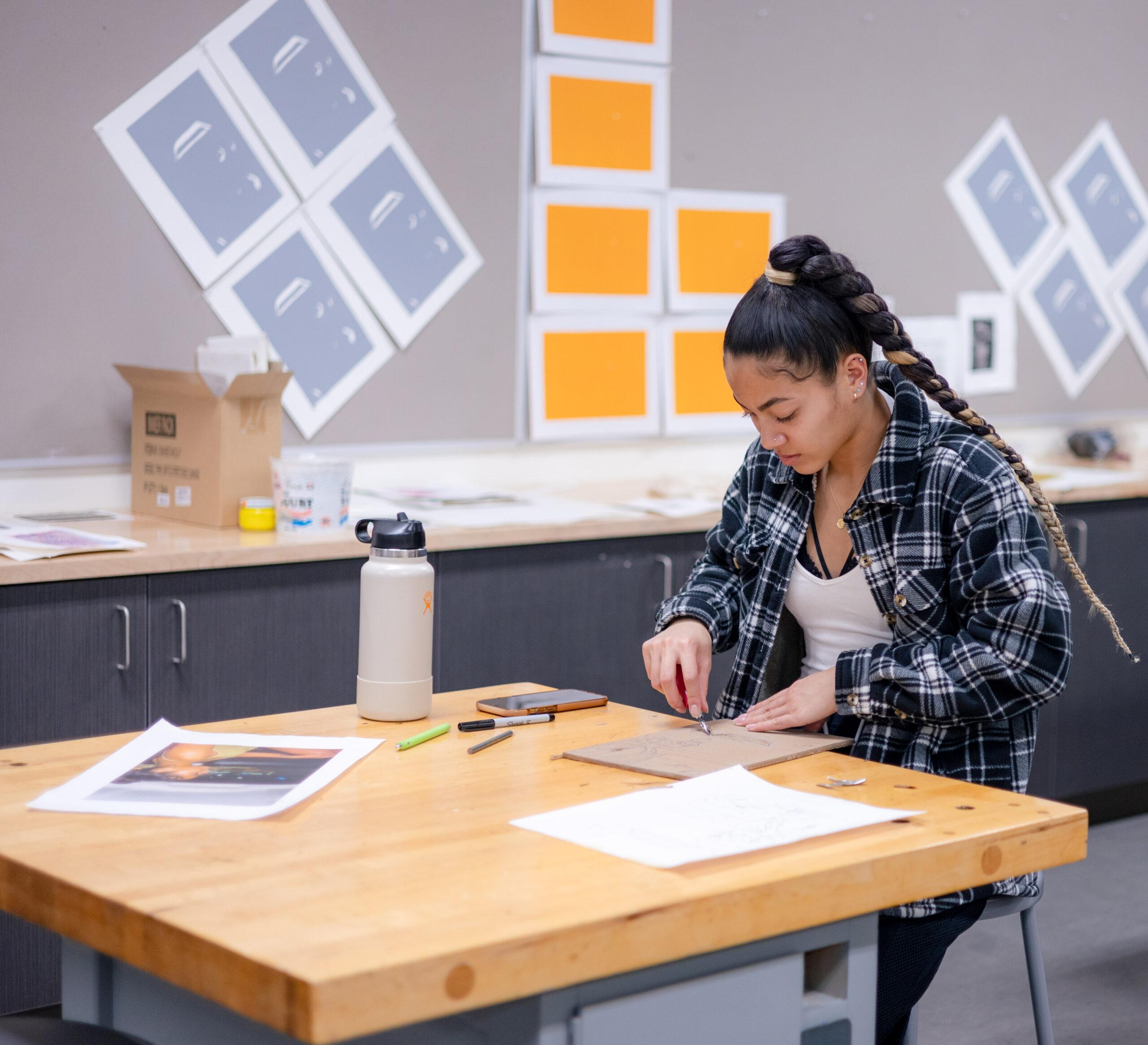 A student is seated and carves a design into a stamp