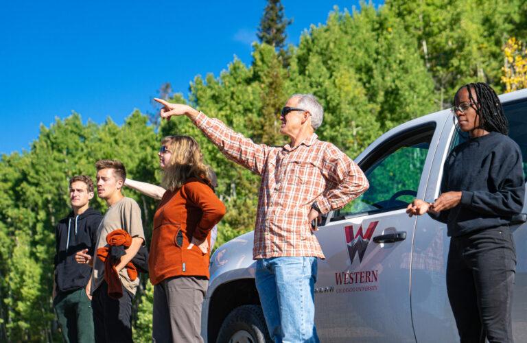 A professor points to an unknown destination in the distance during a field trip.