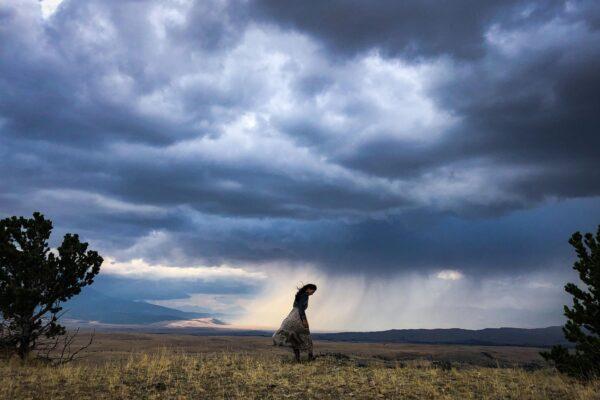 CMarie stands in a prairie field while a storm brews behind her.