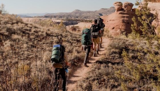 Backpackers hike across a trail in the desert.