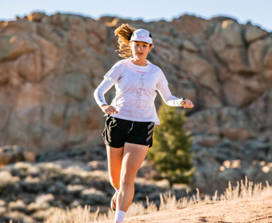 A girl trail runs in her adidas team uniform with with rock formations in the background.