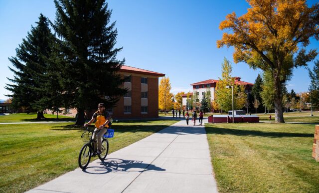 Several students bike and walk across the Western Colorado University campus on a fall day.