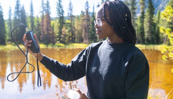 A female student uses a device to test a biological sample from a pond.