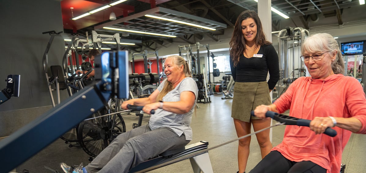 A exercise and sport science student assists two community members in a fitness exercise.
