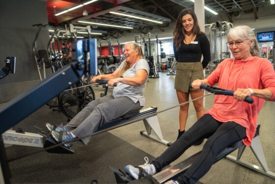 A exercise and sport science student assists two community members in a fitness exercise.