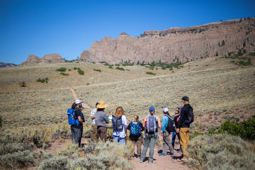 A group of several students listen to a presentation outdoors.