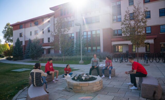 Several students hang out near an outdoor fire pit at the Pinnacles Apartment buildings.