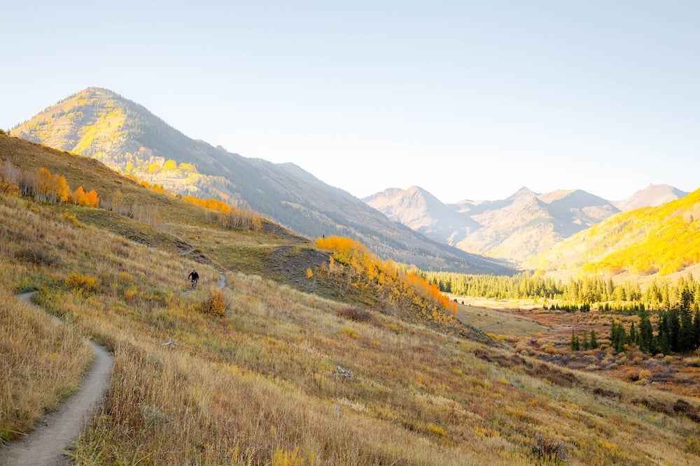 A bright fall landscape in Crested Butte, Colorado, captured in 2025, showcasing golden and orange aspens glowing across the valley beneath rugged mountain peaks.