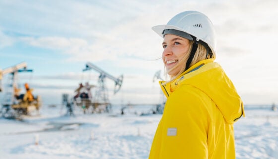 Smiling young engineer wearing hardhat at oil production field in winter