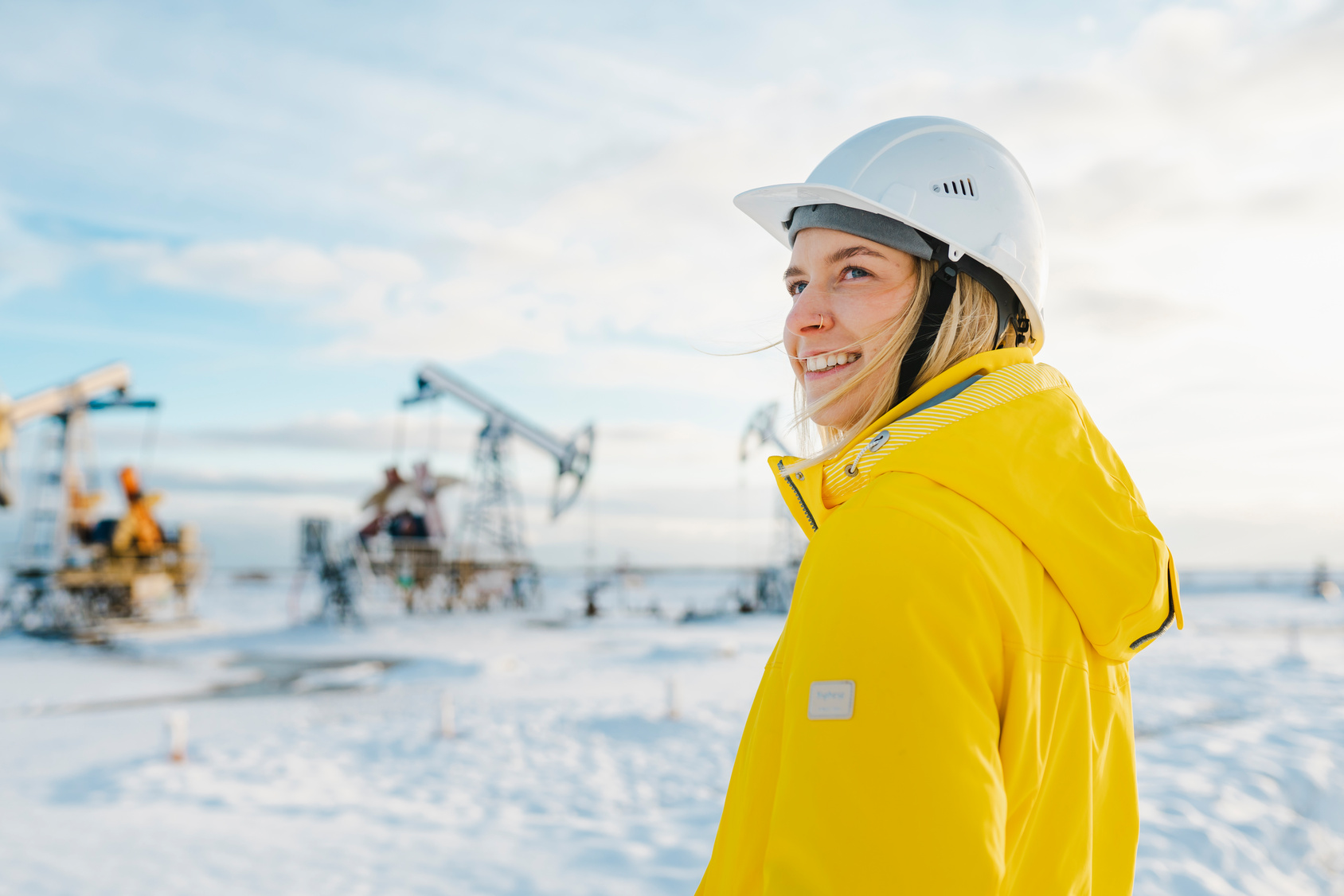 Smiling young engineer wearing hardhat at oil production field in winter