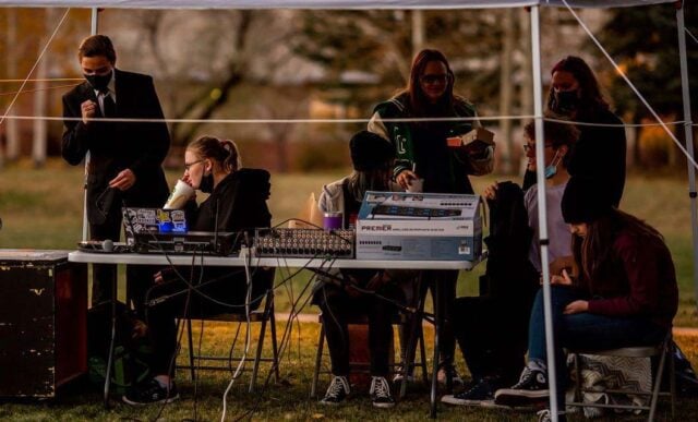 Students are seated under a tent working stage sound and lighting.