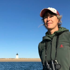 Elizabeth Bradfield stands in front of a bay with binoculars.