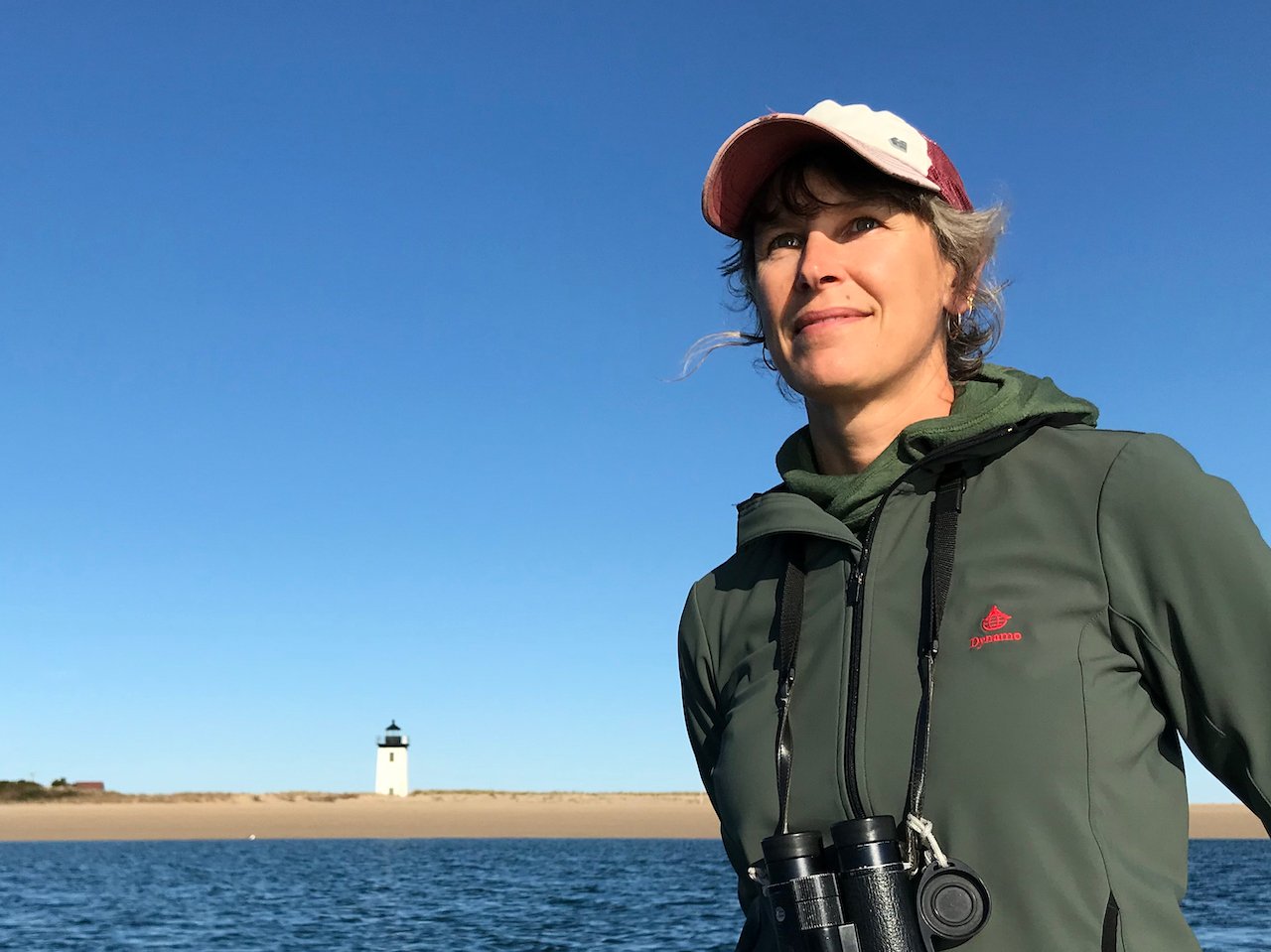 Elizabeth Bradfield stands in front of a bay with binoculars.