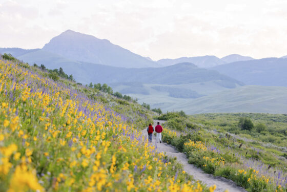 Two students wearing red jackets walk the East River Trail at sunrise during wildflower season.