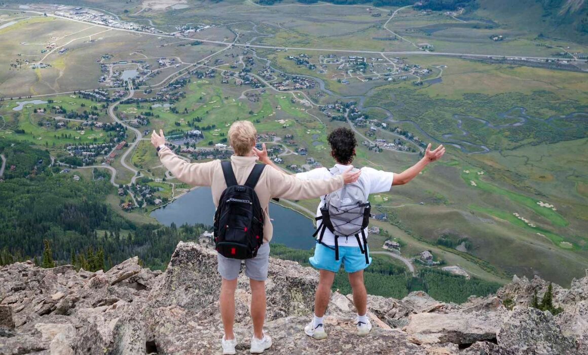 Two students hold their arms out while taking in big views of Whetstone on their way up to the top of Mt. Crested Butte.