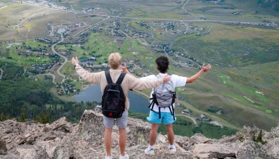 Two students hold their arms out while taking in big views of Whetstone on their way up to the top of Mt. Crested Butte.