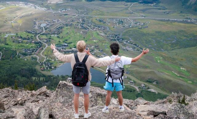 Two students hold their arms out while taking in big views of Whetstone on their way up to the top of Mt. Crested Butte.