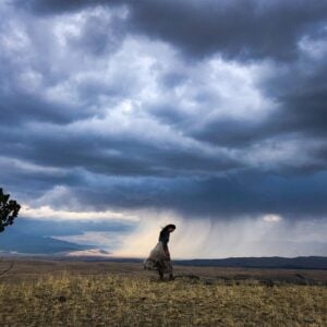 CMarie Fuhrman in a field of grass with a storm brewing behind her.