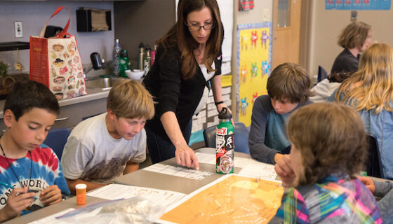 Dr. Jessica Laramie helps a group of fifth grader add up the environmental costs of the pretend power plants they built in the game.