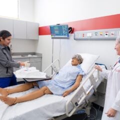 Nursing faculty, Mary Sawyer observes while a student puts on gloves before working with a mannequin in the simulation lab.