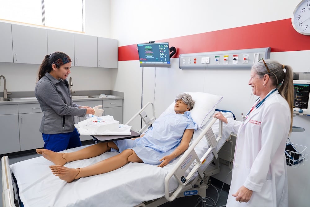 Nursing faculty, Mary Sawyer observes while a student puts on gloves before working with a mannequin in the simulation lab.