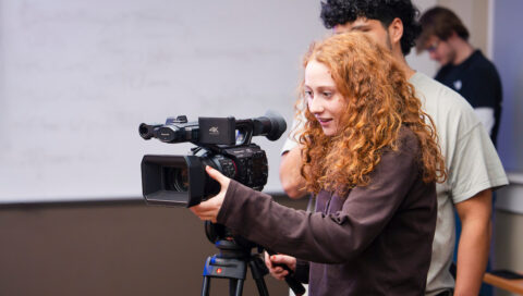 A student practices framing different types of camera shots during an Intro to Film Studies course.