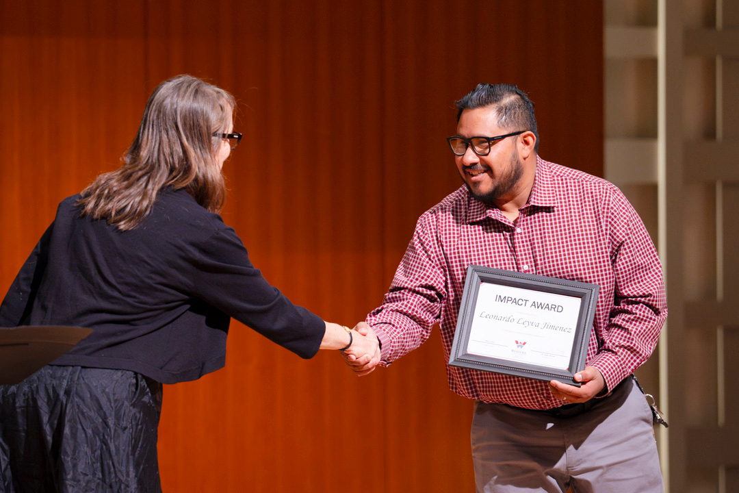 Leonard Leyva Jimenez and Kelsey Bennett shake hands as she presents him with an award for graduate studies.