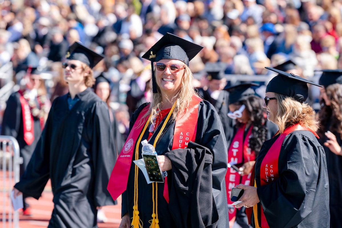 An adult degree completion program graduate smiles big as she takes a seat during commencement.