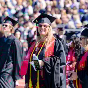 An adult degree completion program graduate smiles big as she takes a seat during commencement.