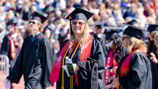 An adult degree completion program graduate smiles big as she takes a seat during commencement.