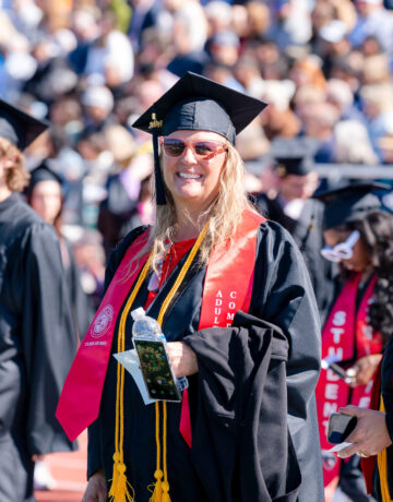 An adult degree completion program graduate smiles big as she takes a seat during commencement.