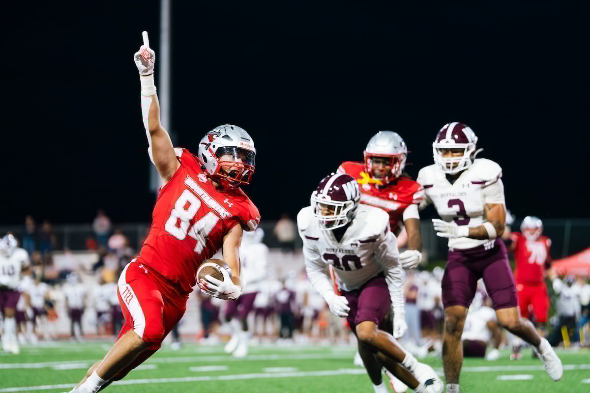 Football player number 84 holds his finger in the air as he runs the ball into the touchdown zone in a game against West Texas A&M.