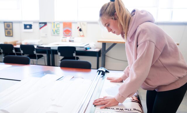A graphic design student trims the edges of a poster she made to get ready for a class critique.