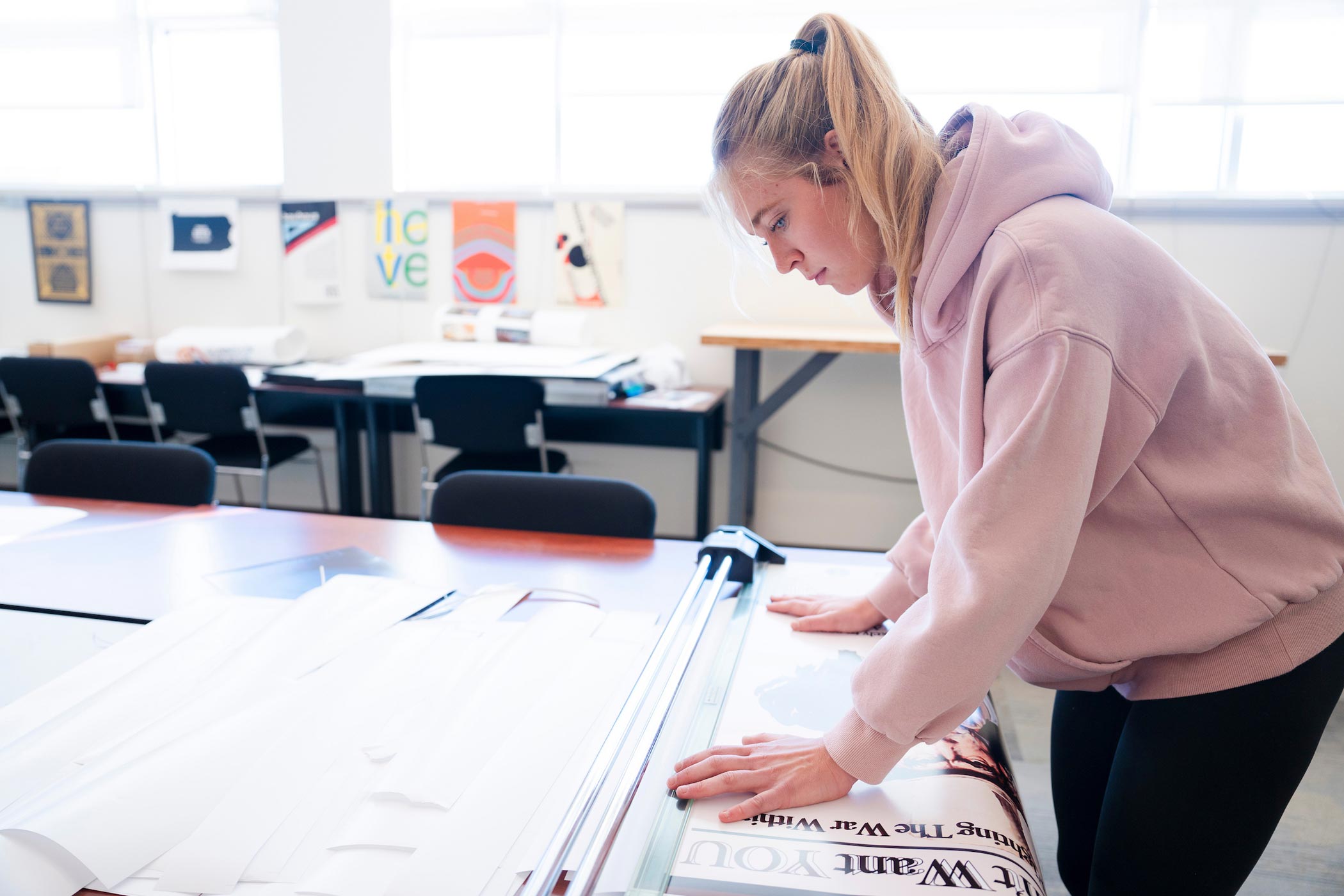 A graphic design student trims the edges of a poster she made to get ready for a class critique.