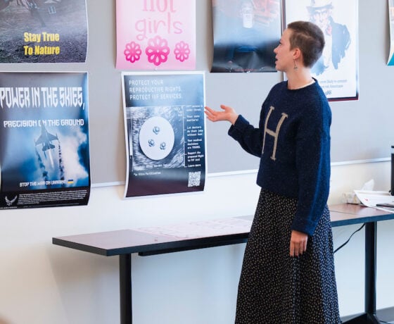 A graphic design student stands in front of a class and gives them an overview of a poster she designed during a critique.