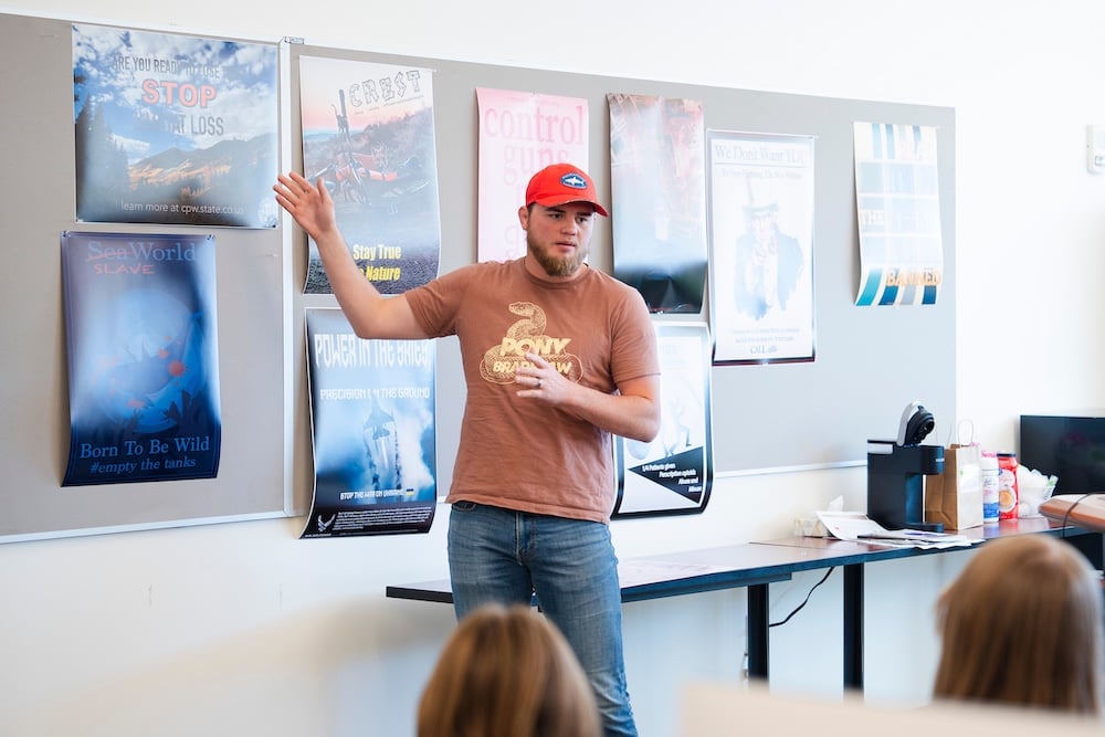 A graphic design student stands in front of a class and gives them an overview of a poster he designed during a critique.